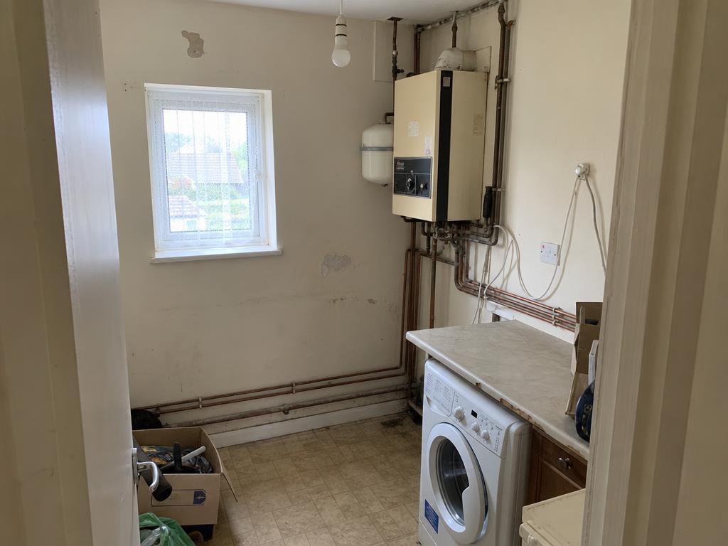 Outdated laundry room with exposed corroded pipes before renovation